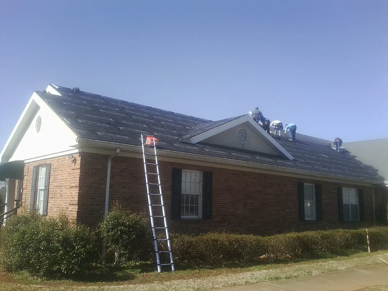 Crew tearing shingles off a brick ranch roof with a ladder set — Emergency Roof Repair work by our crew in Lockeford