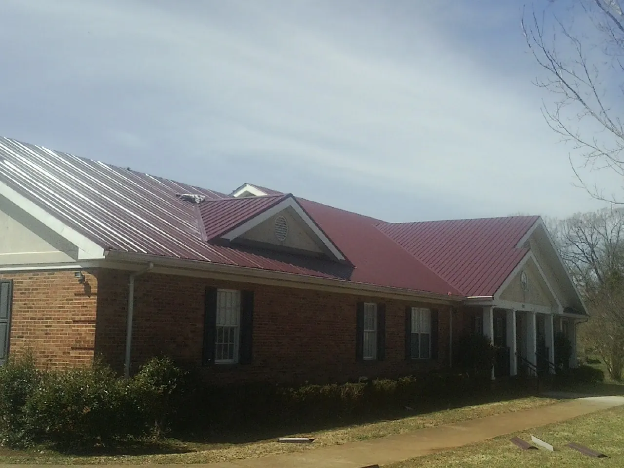 Red metal roof with gabled entries on a long brick building, from a Hail Damage Roof Repair job in Lockeford