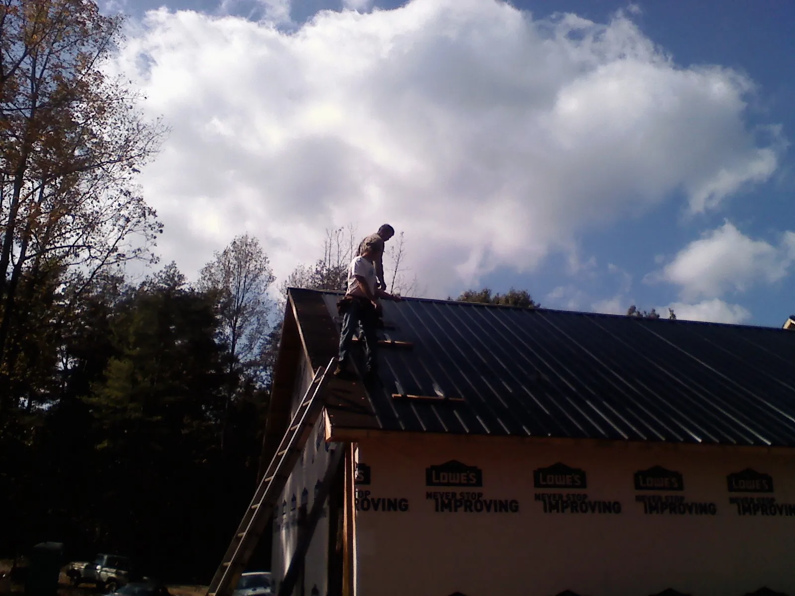 Roofer fastening dark metal panels high against a cloudy sky, from a Roof Inspection job in Lockeford