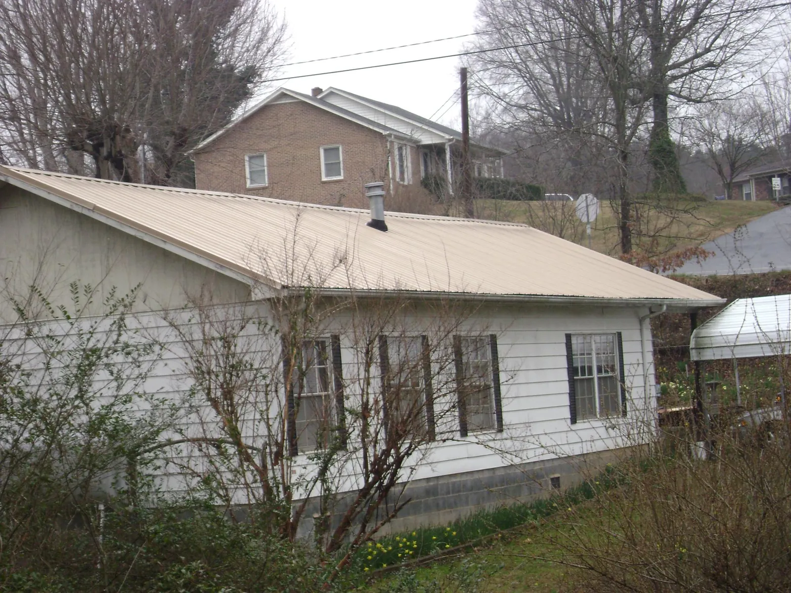 Tan metal roof on a white sided house set into a hillside — Commercial Roofing by Roofing Brothers in Lockeford